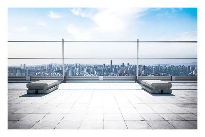 Betongegengewichte auf einer Dachterrasse, dahinter Geländer und Stadtsilhouette